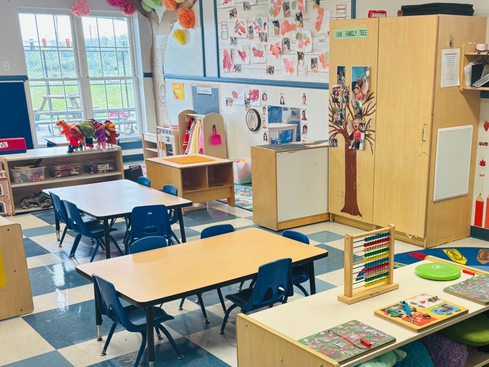 An empty classroom with small tables and chairs, toys, and crafts on the walls