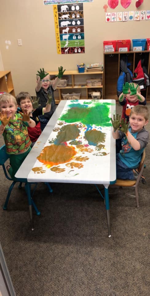 Children with painted hands around a table with paint handprints