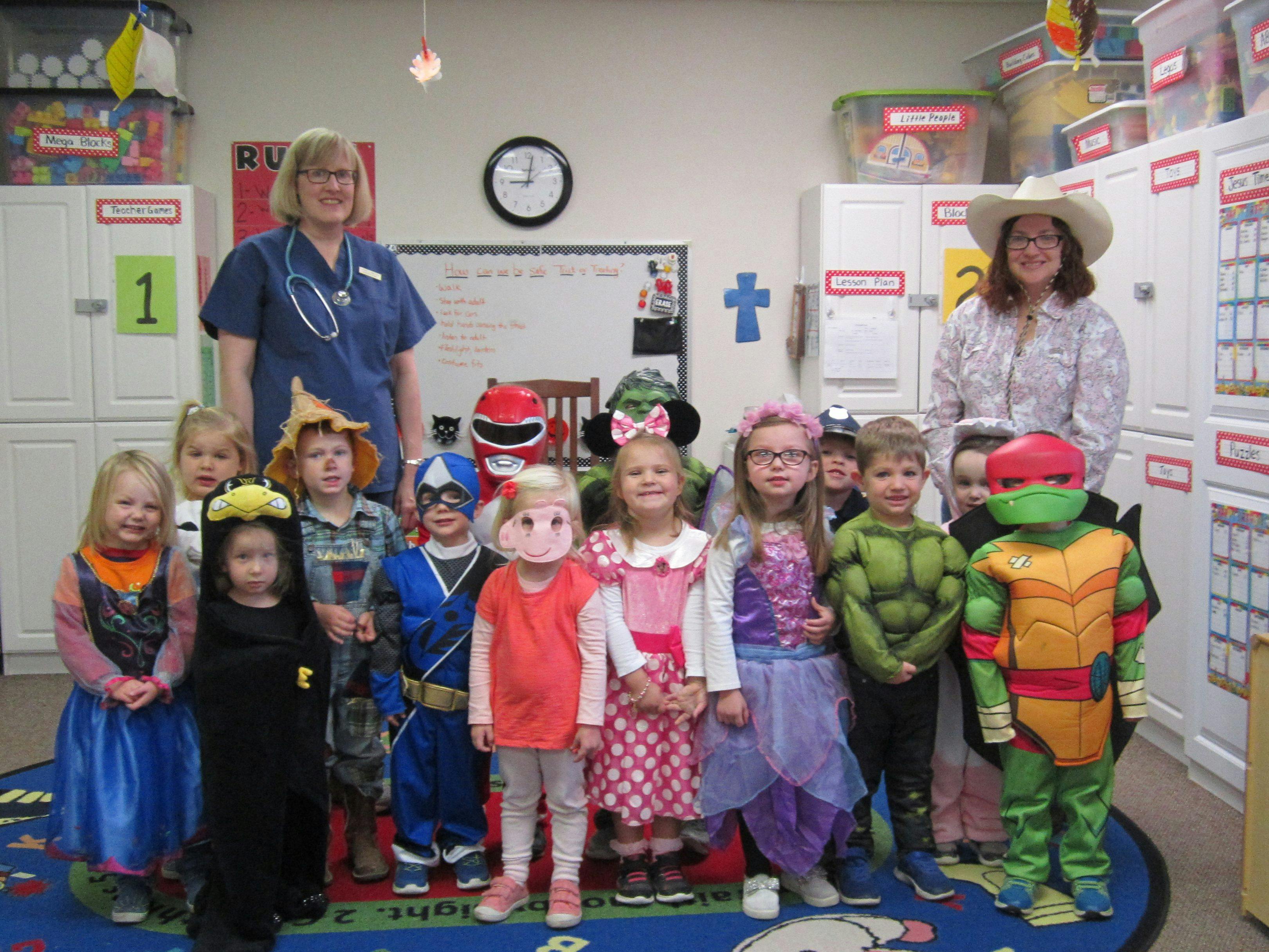 Two adults and multiple children in costumes standing in a classroom