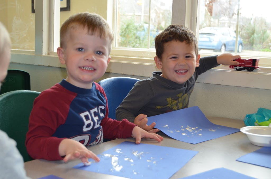 Two children sitting at a table with blue papers