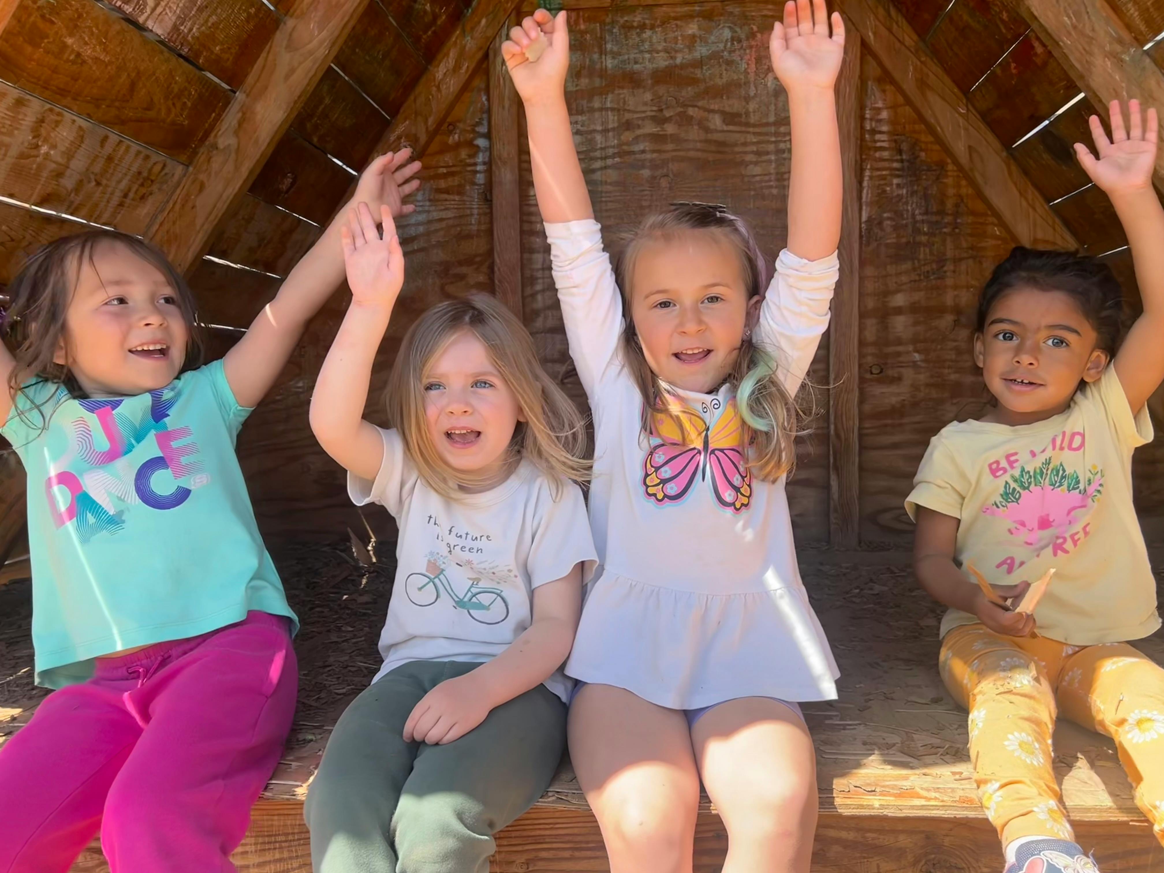 Four children sitting with their arms raised