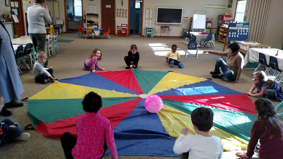 Children and adults sitting around a colorful parachute with a pink ball