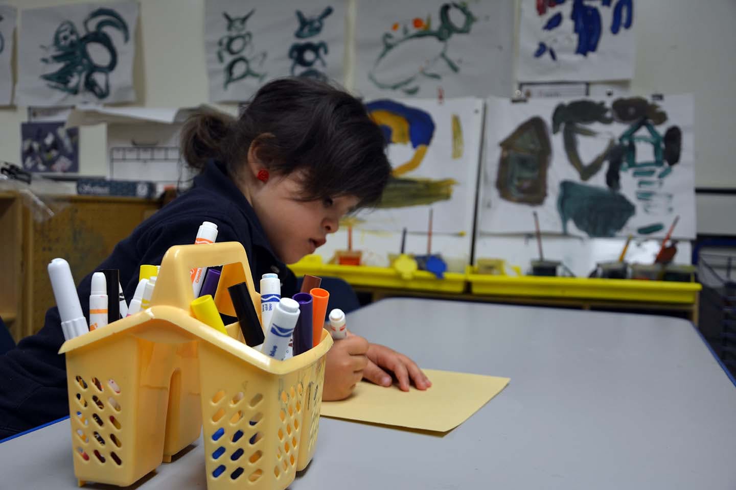 Child drawing at a table with a caddy of markers