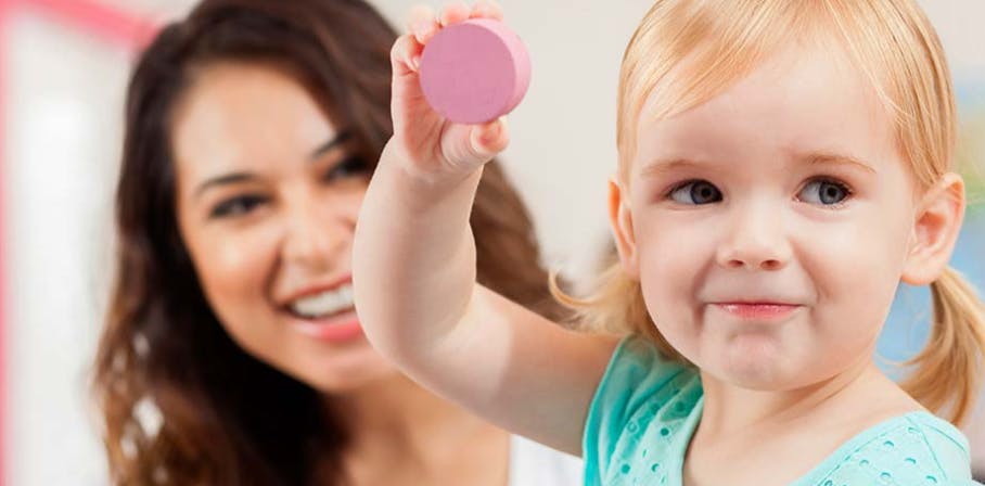 Child holding up a pink toy with a person smiling in the background