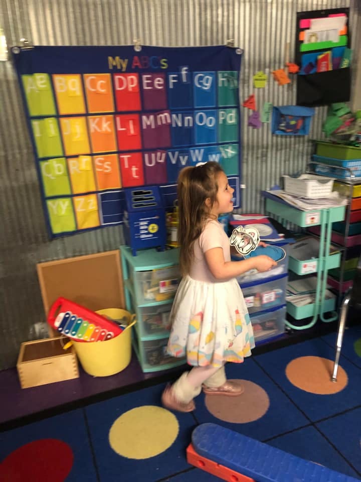 Child walking in a classroom with an alphabet chart on the wall