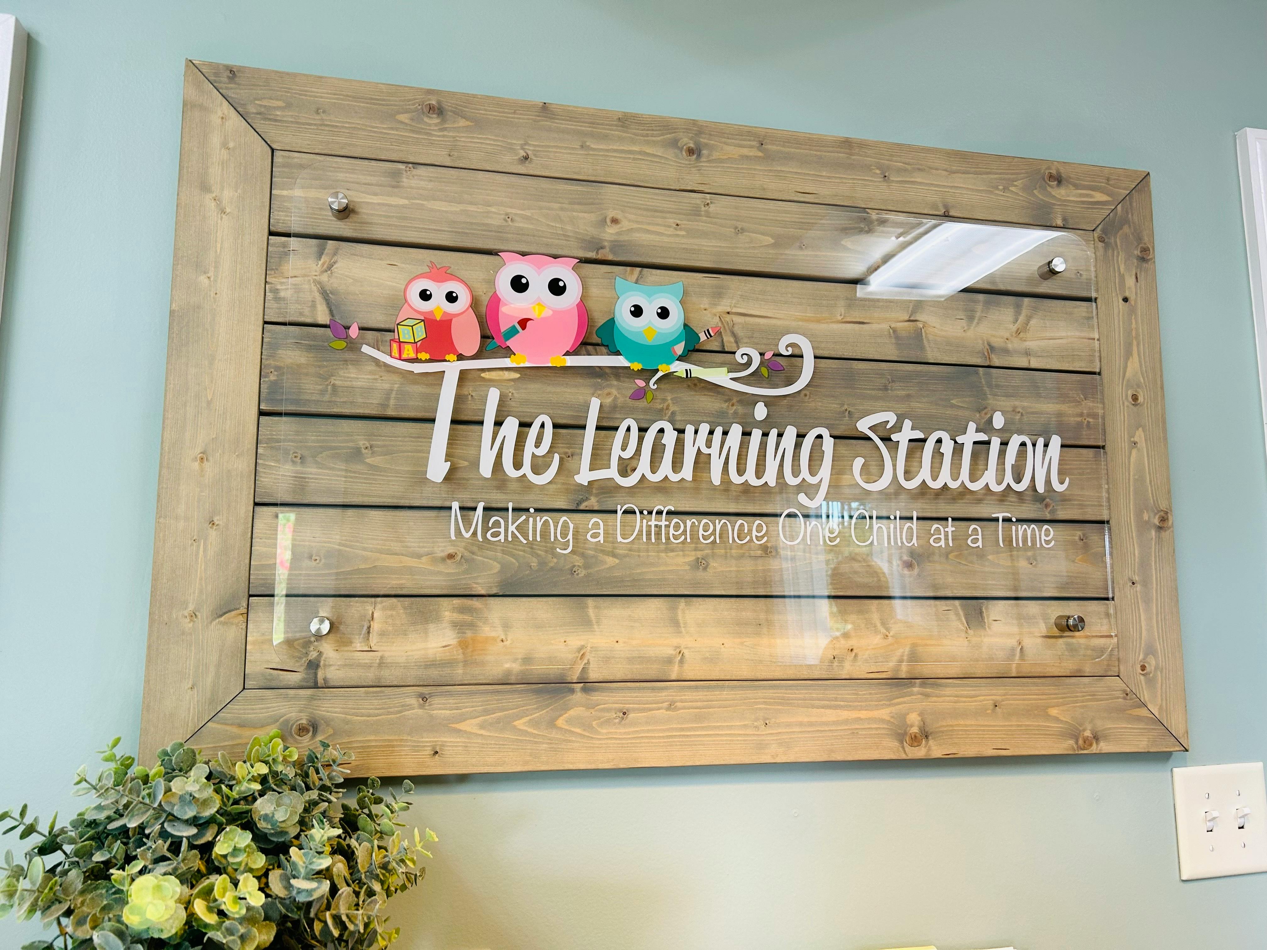 Wooden sign with three cartoon owls and text "The Learning Station"