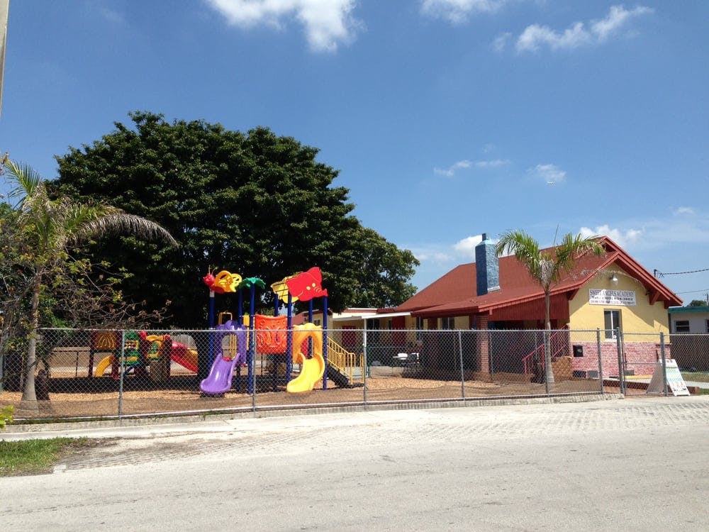 Playground with slides and swings behind a fence, next to a building