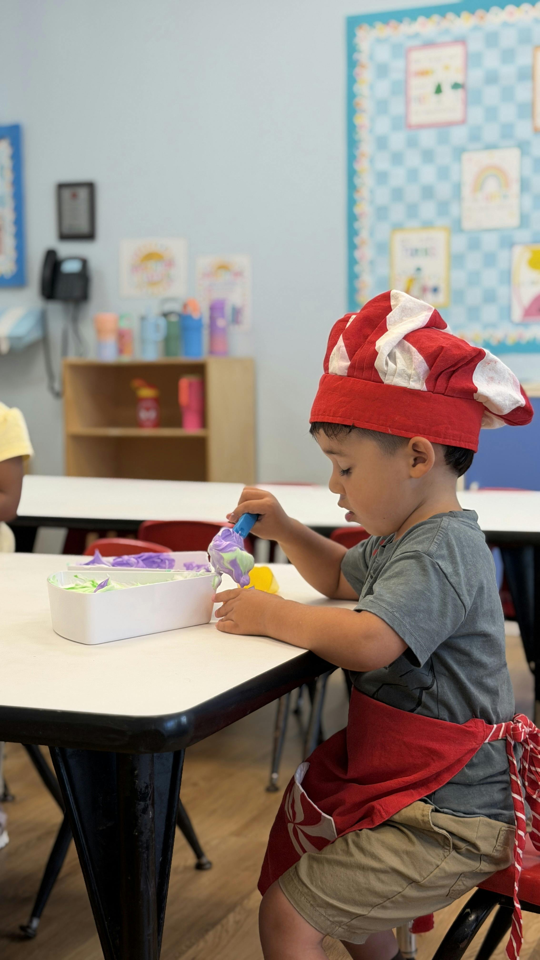 Child wearing a chef hat and apron playing with colored foam at a table