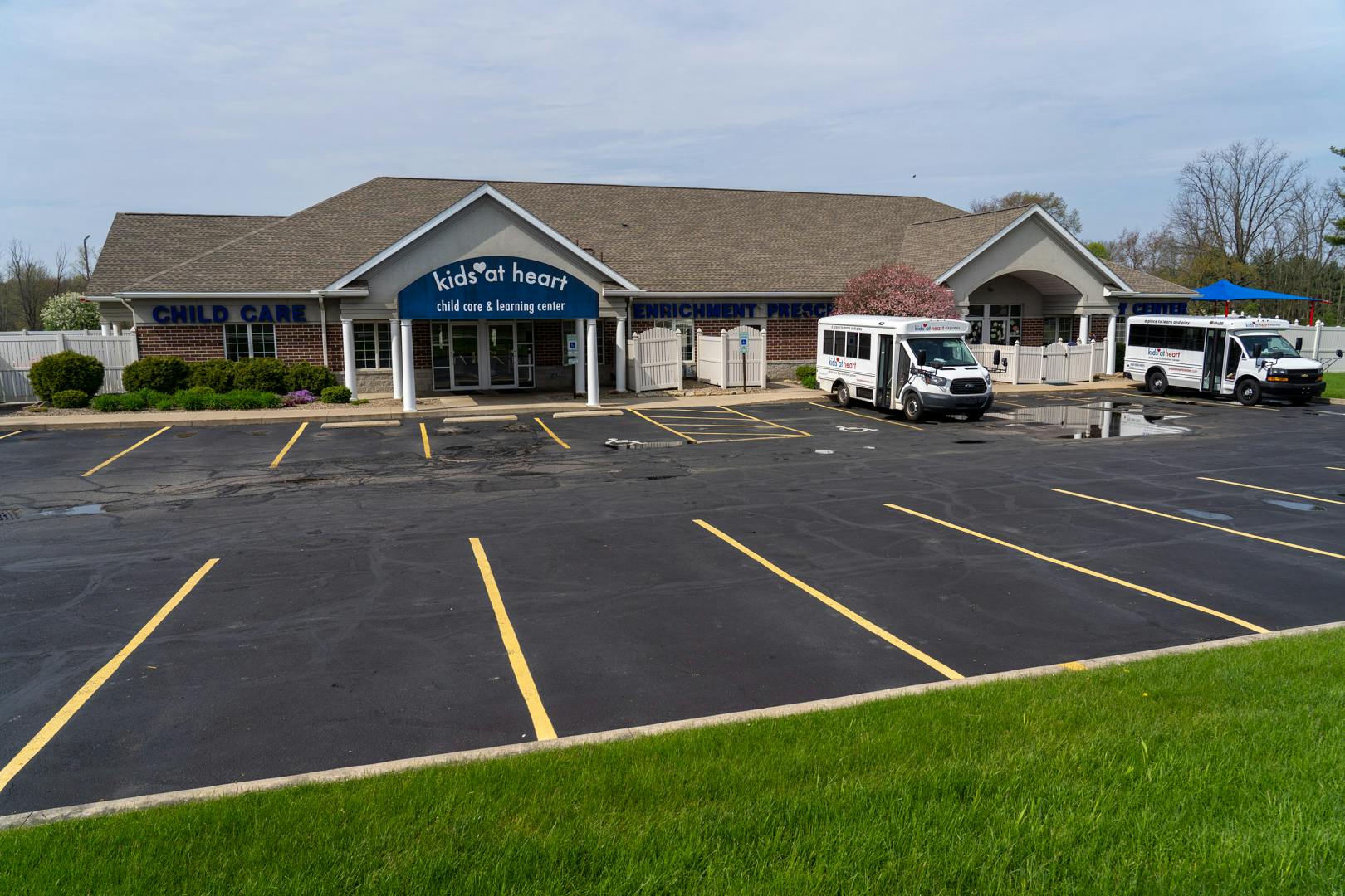 Building with a sign that reads "Kids' Play House" and two white buses in the parking lot