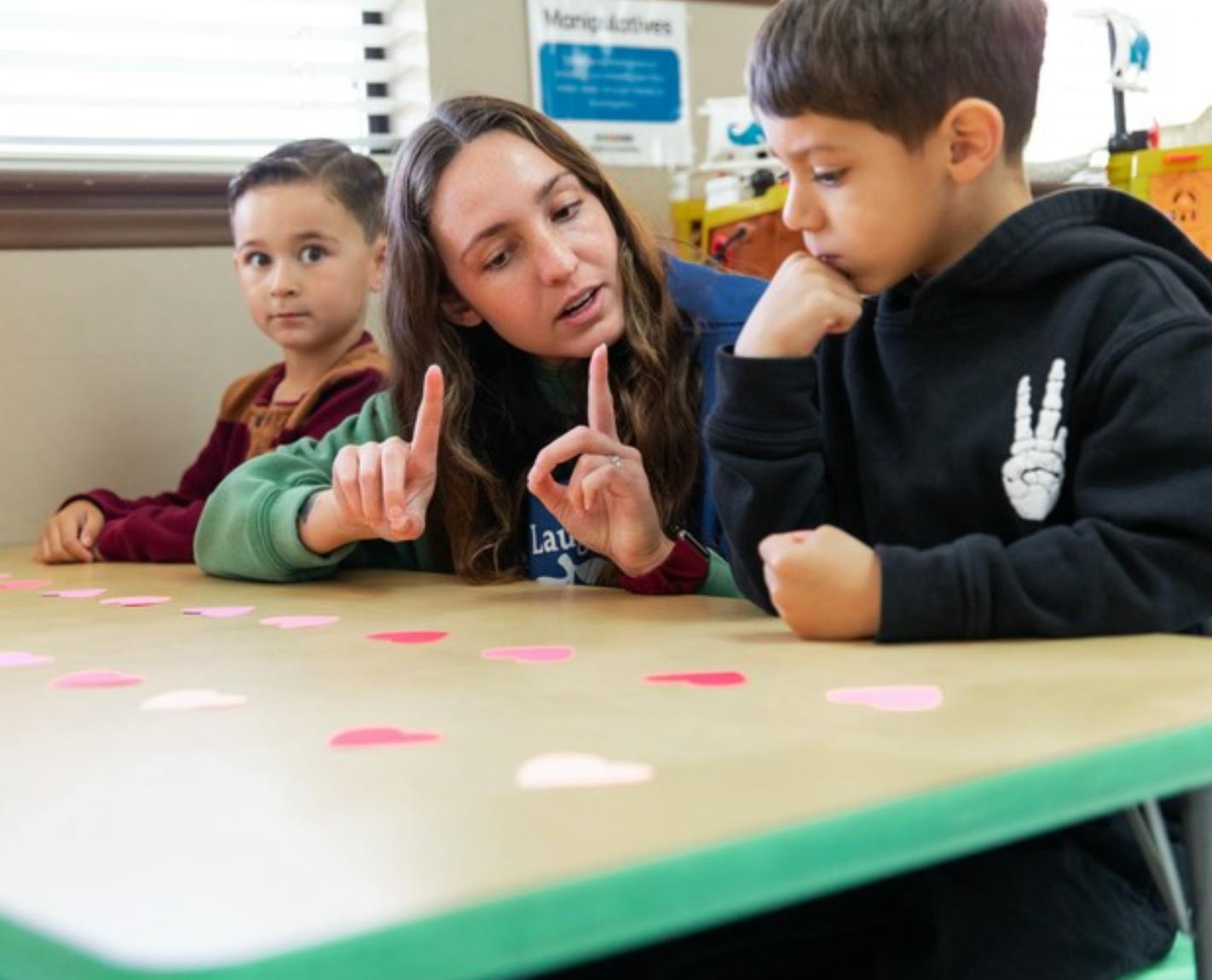Teacher and two children at a table with paper hearts
