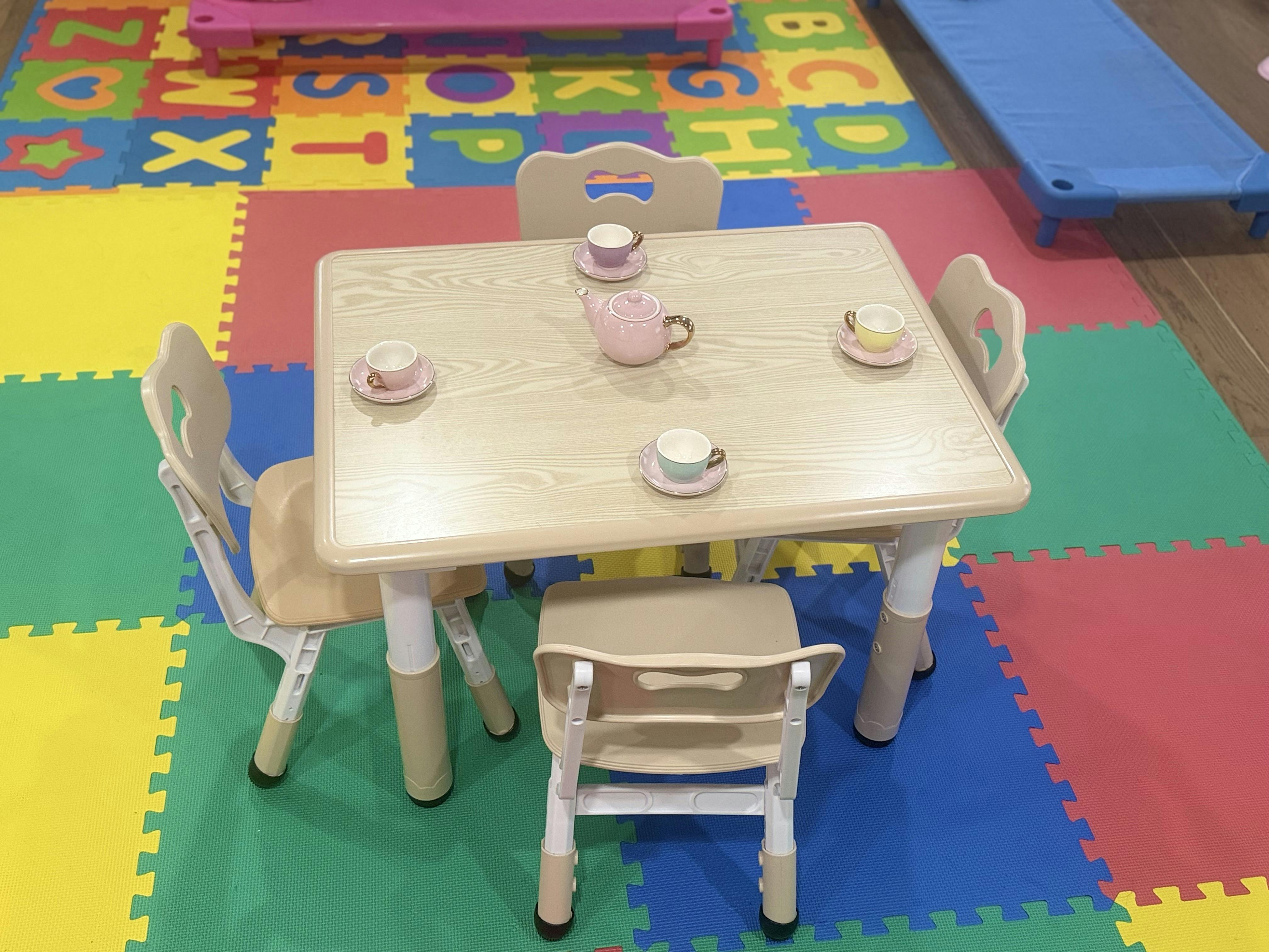 Children's table and chairs with a toy tea set on a colorful alphabet mat
