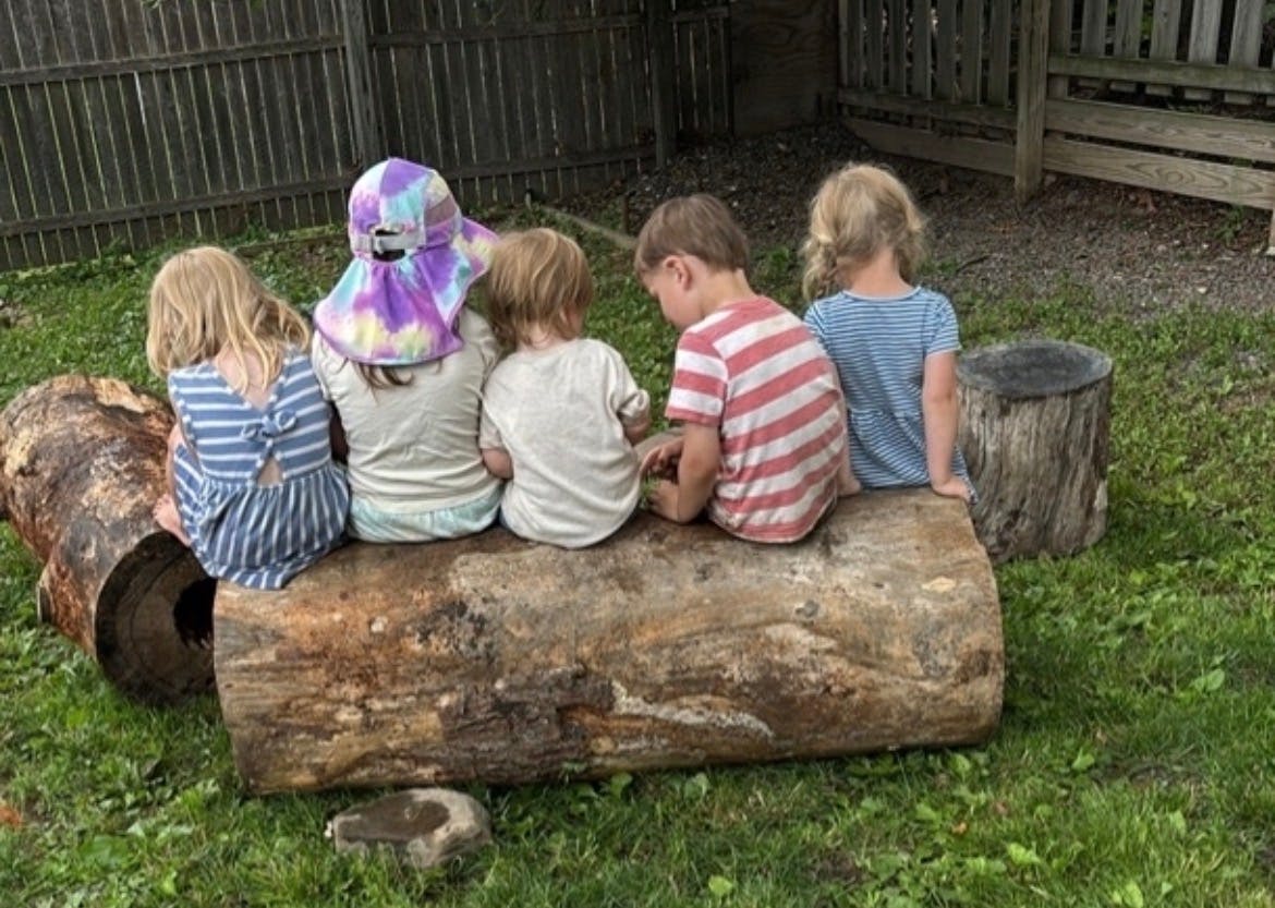 Five children sitting on a log outdoors
