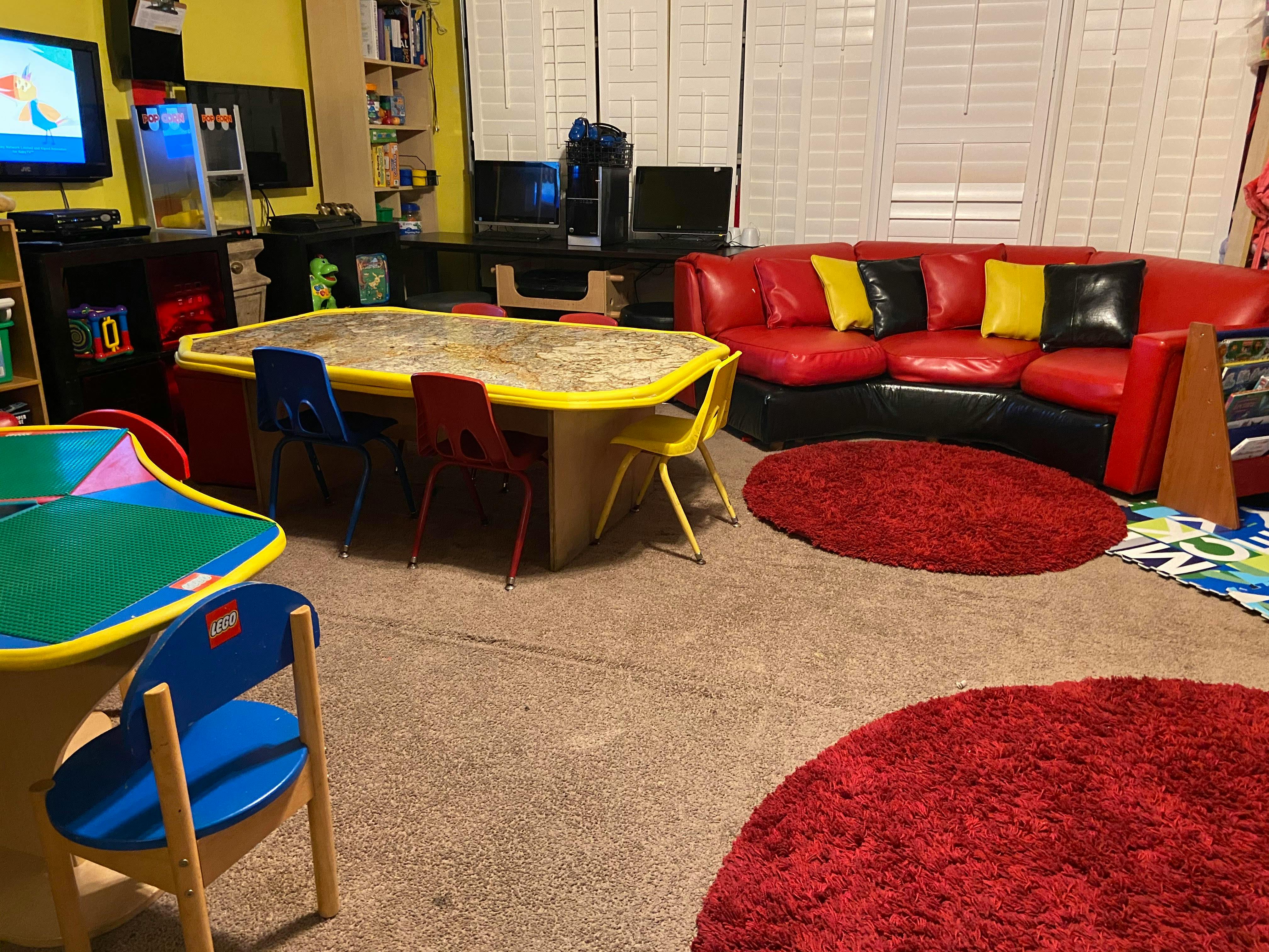 Playroom with a red couch, two tables with chairs, and red rugs