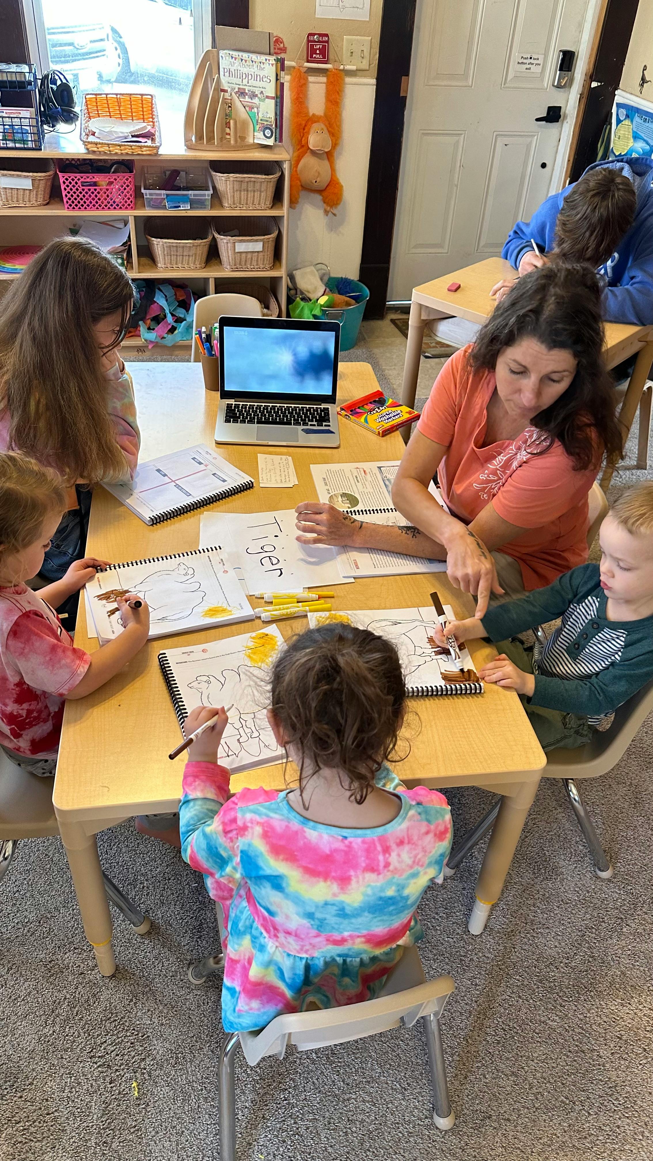 Adult and children drawing at a table in a classroom
