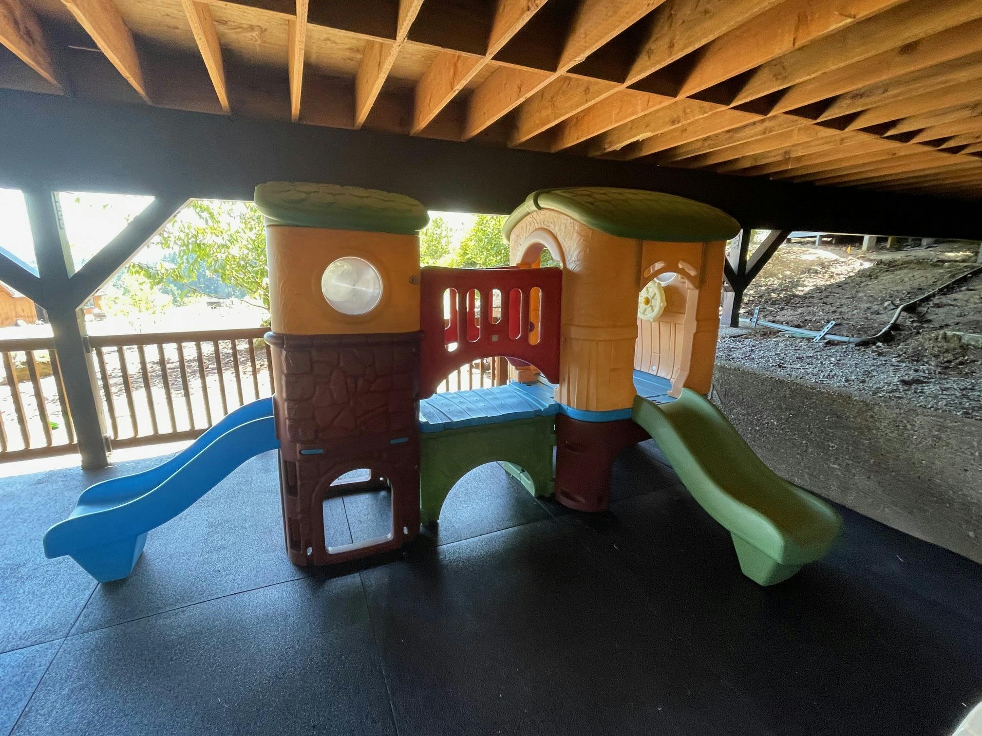 Children's play structure with slides under a wooden deck