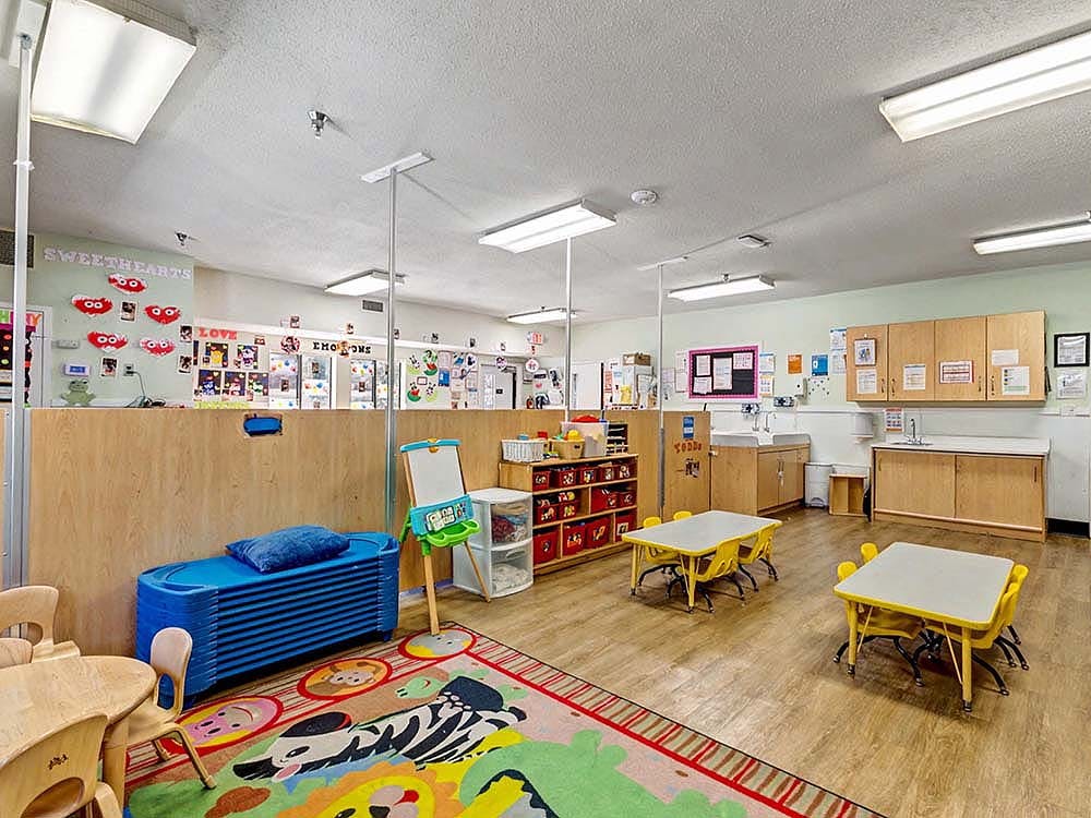 Colorful classroom with child-sized tables, chairs, a rug, and storage units