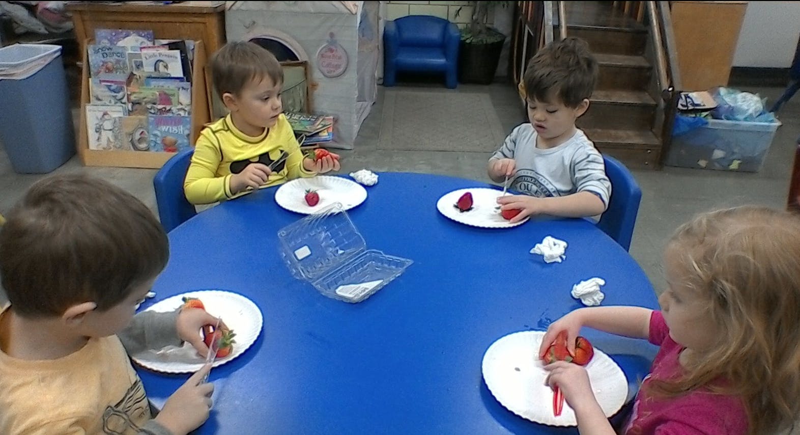 Four children sitting at a table with plates of strawberries