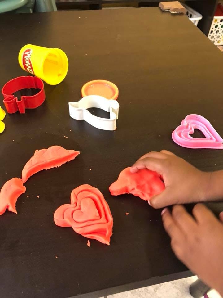 Child's hands playing with red playdough and cookie cutters