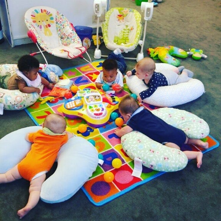 Multiple babies playing on a colorful mat with toys