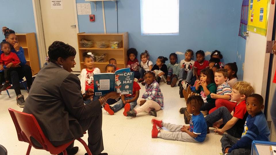 Person reading "The Cat in the Hat" to a group of children in a classroom