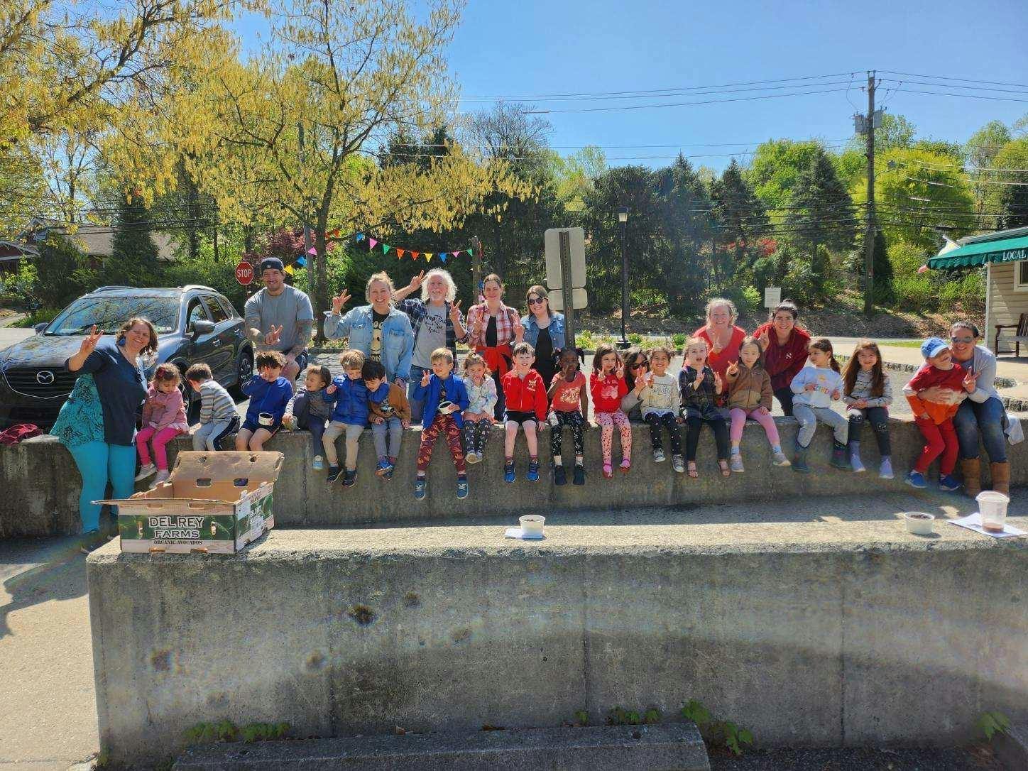 Group of adults and children sitting on a concrete ledge outdoors