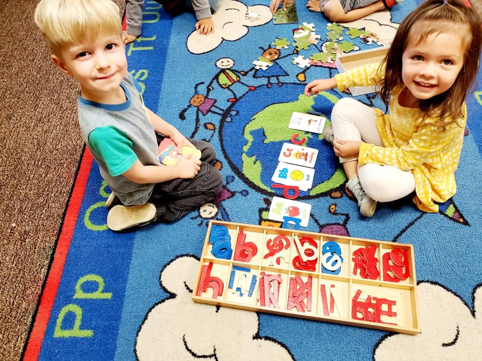 Two children playing with learning materials on a rug