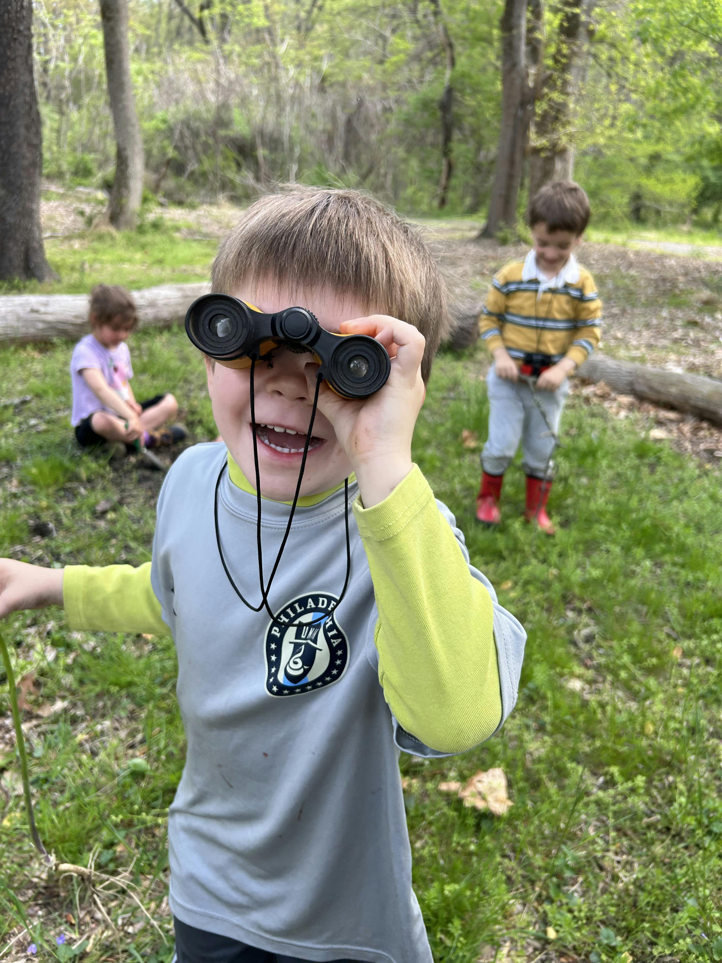 Child looking through binoculars with two other children in background