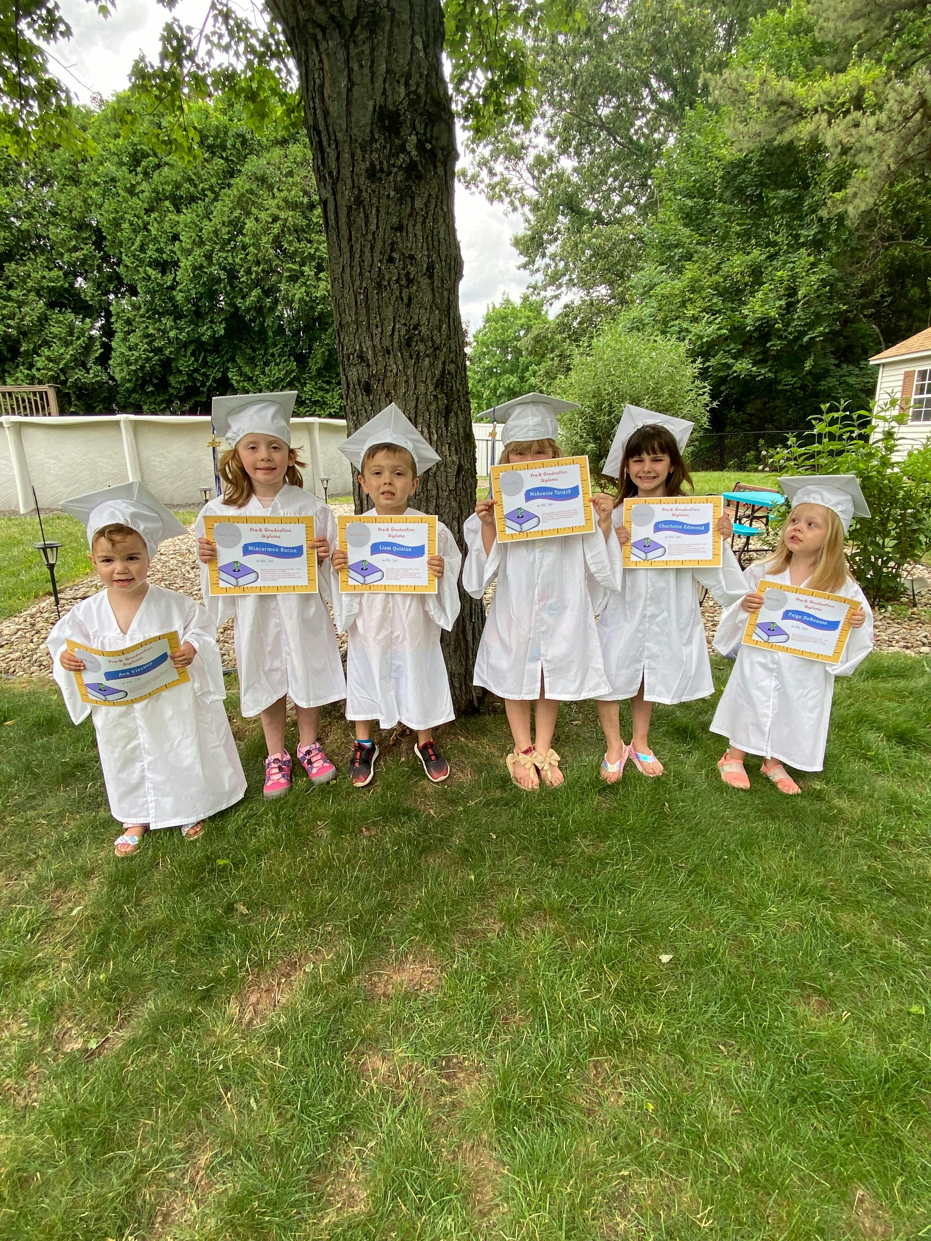 Six children in graduation caps and gowns holding certificates