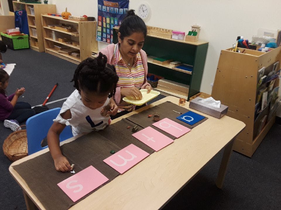 Adult and child working with letter cards at a table in a classroom