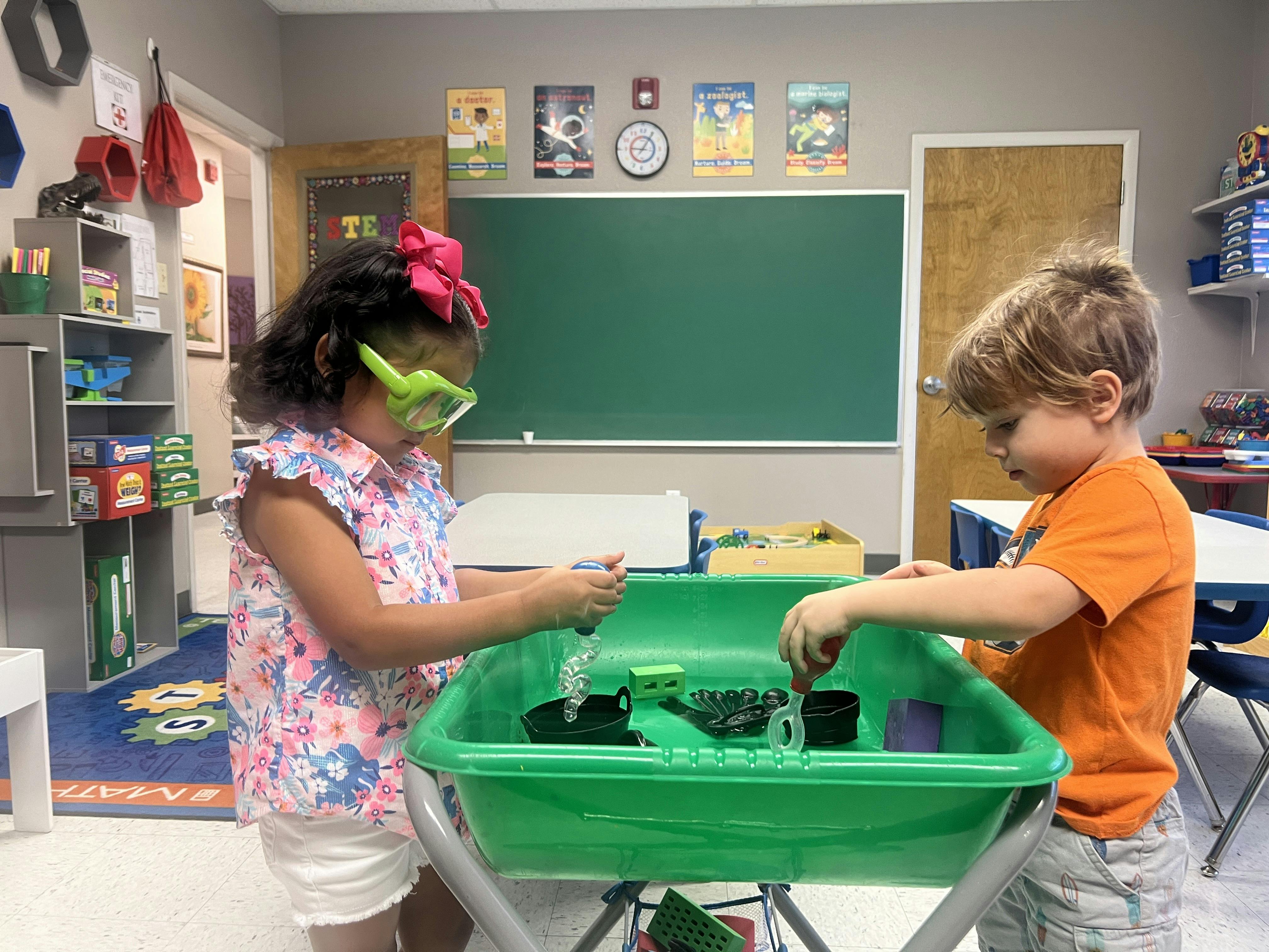 Two children playing with toys in a green sensory bin in a classroom