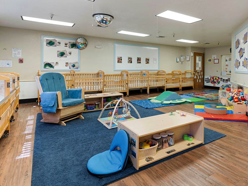 Empty nursery with several cribs, a rocking chair, and play mats on the floor