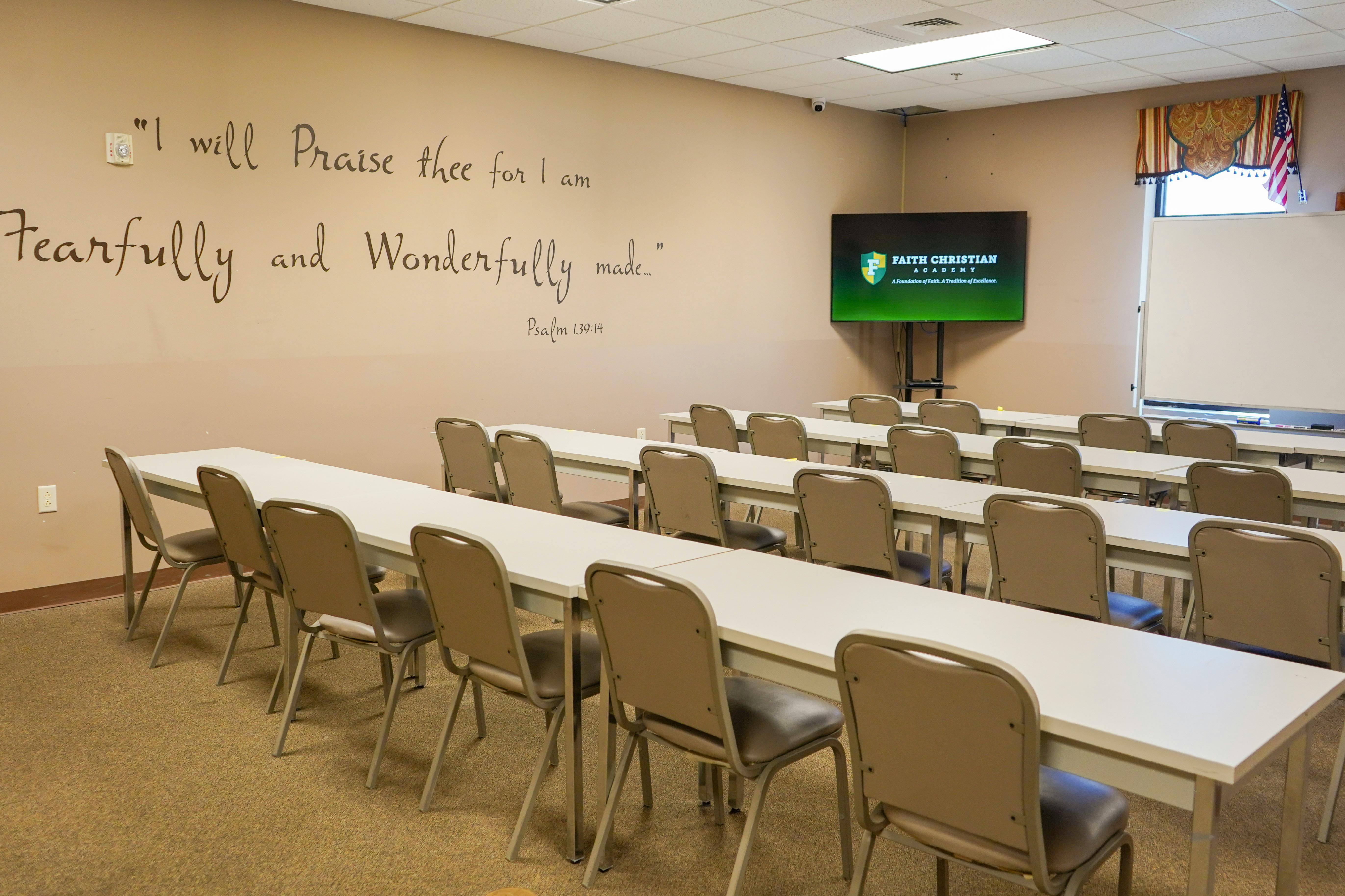 Empty classroom with rows of tables and chairs facing a screen
