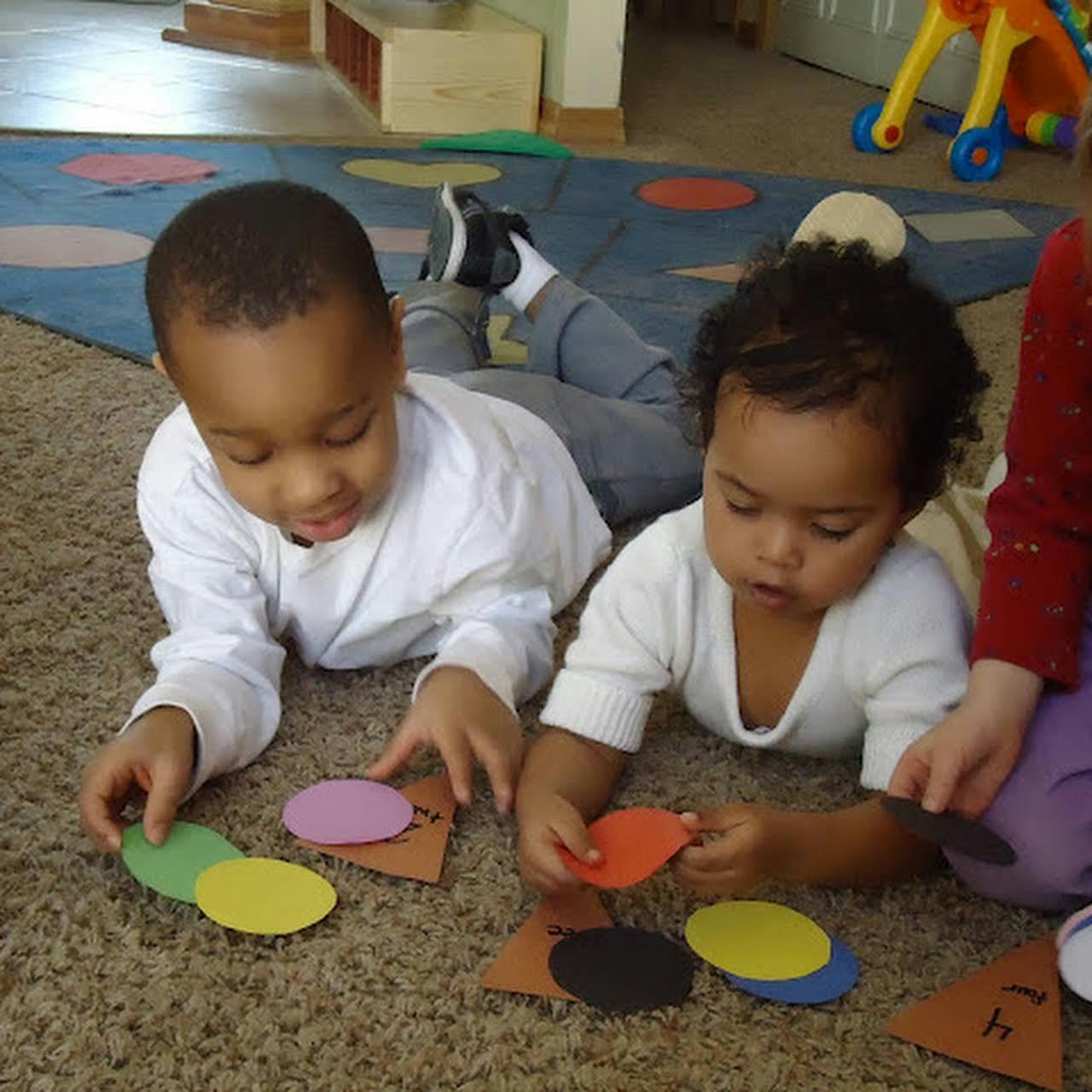 Two children lying on a carpet playing with colorful shapes