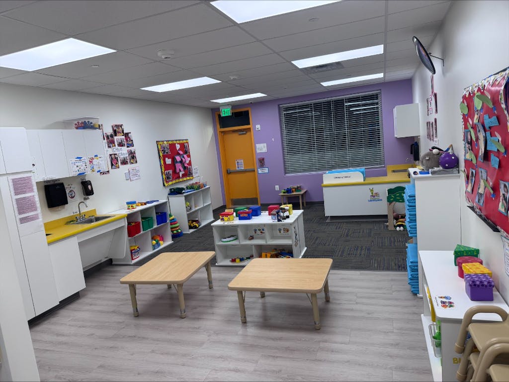 Empty classroom with small tables and shelves of toys