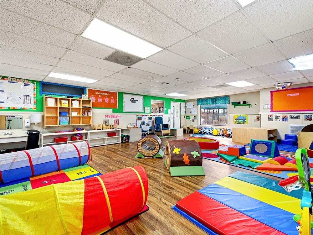 Colorful playroom with soft mats, play tunnels, and shelving along the walls