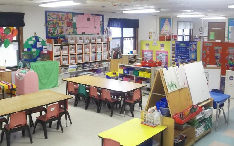 Classroom with child-sized tables and chairs, shelves, and colorful artwork on walls