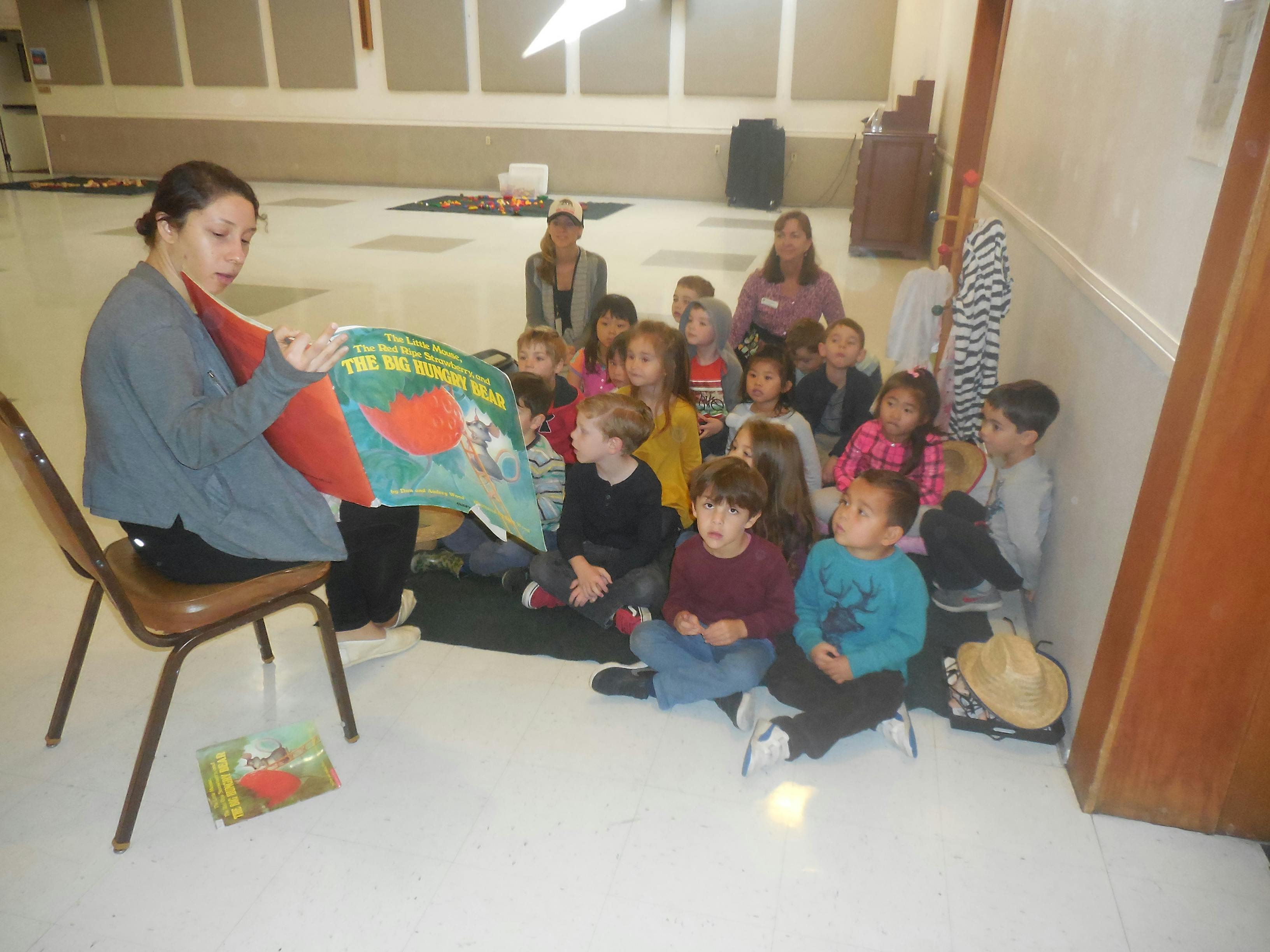 Person reading a book to a group of children sitting children