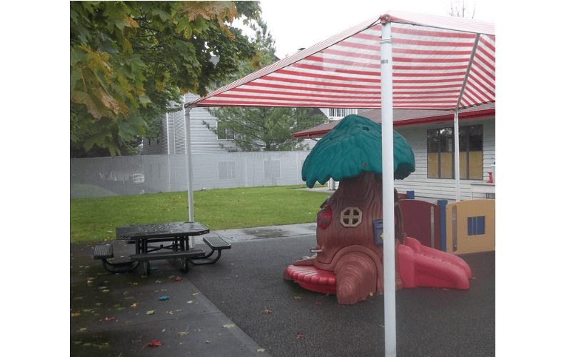 Picnic table and outdoor play equipment under a striped awning