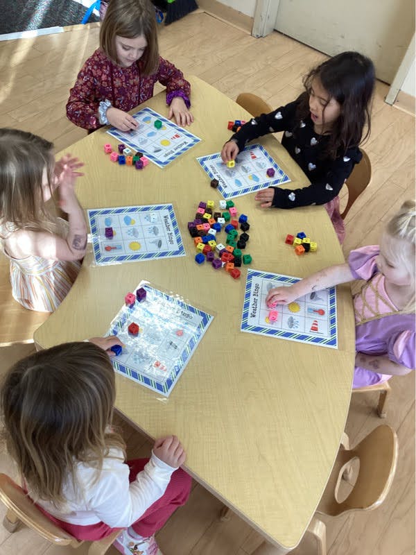 Children playing "Weather Bingo" with colorful blocks in a classroom