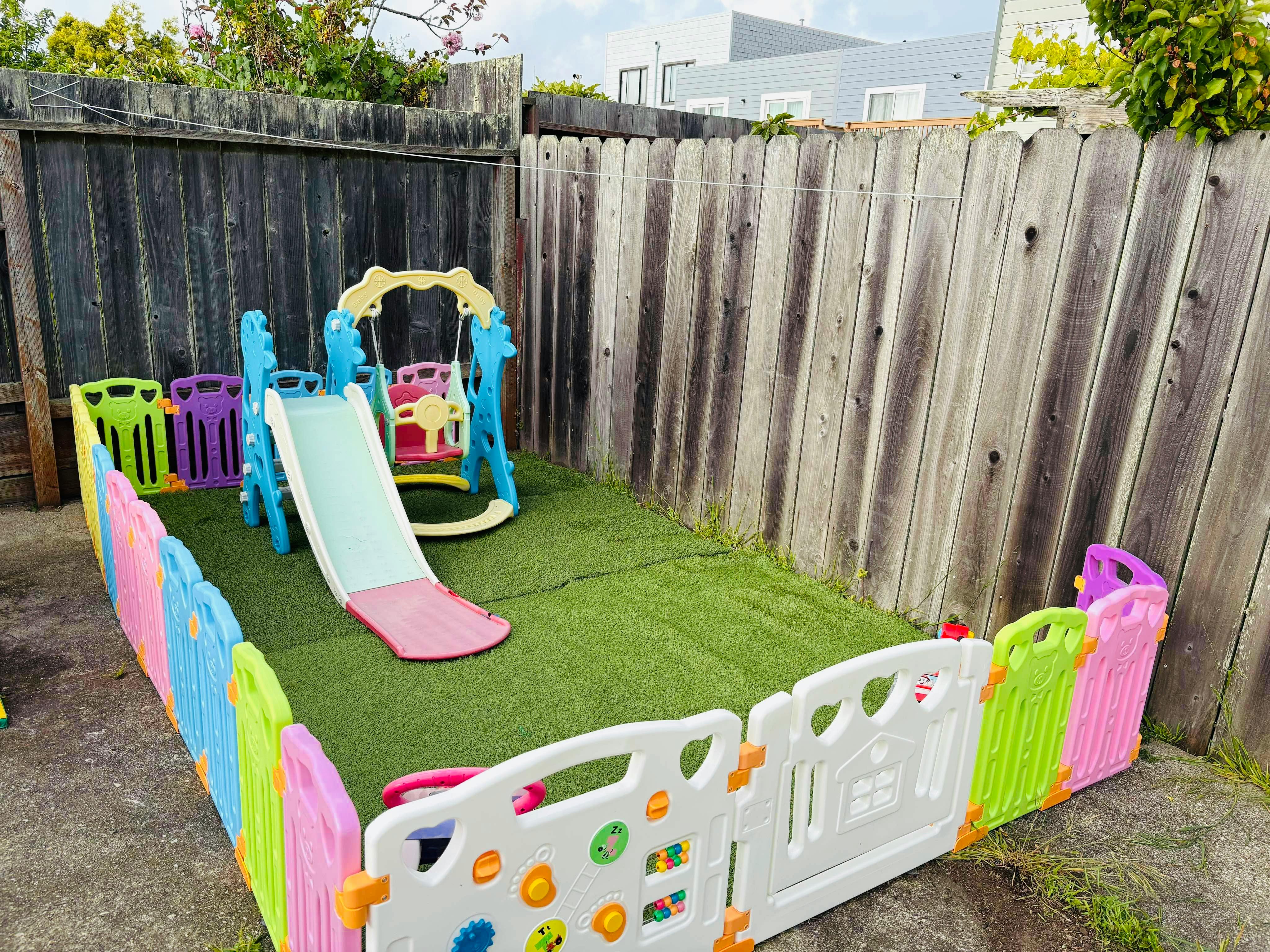Play area with a slide and swing set surrounded by a colorful fence