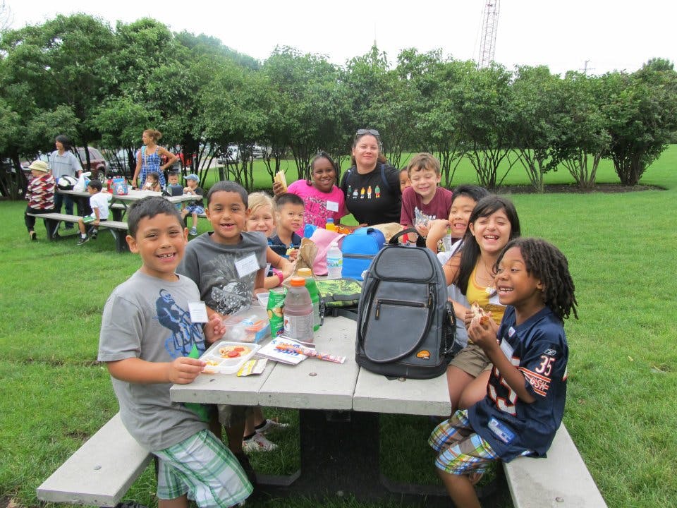 Group of children and adults sitting at picnic tables outdoors