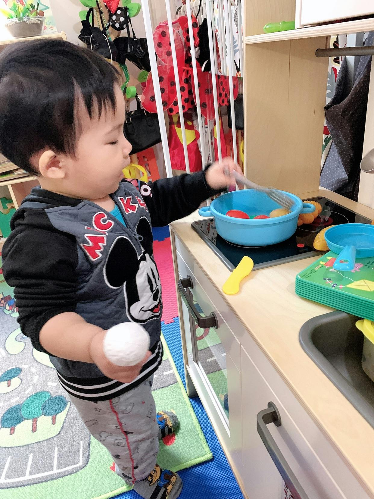 Child playing with toy kitchen set, holding a white ball