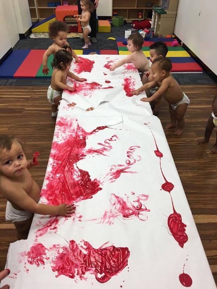 Multiple children finger painting with red paint on a long sheet of paper