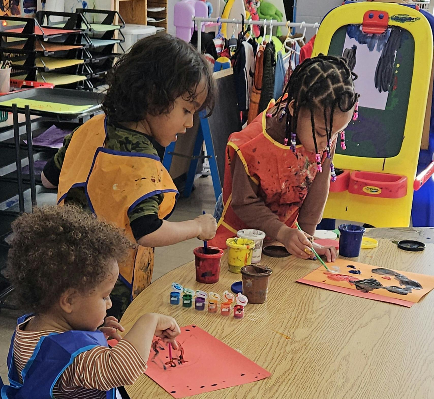 Three children painting at a table in a classroom