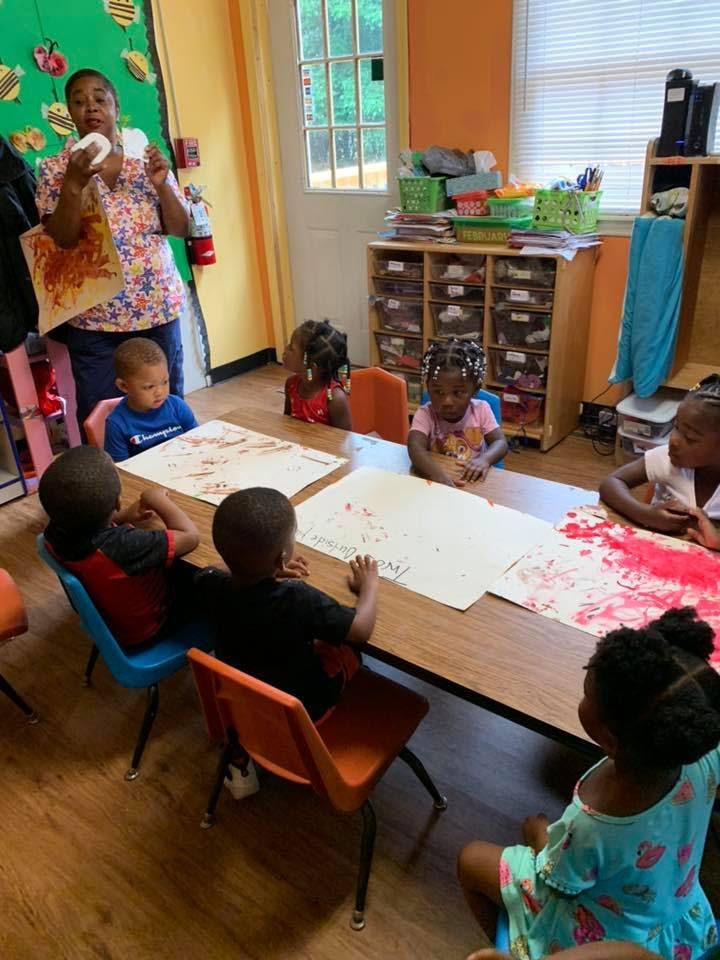 Adult showing children a craft project in a classroom