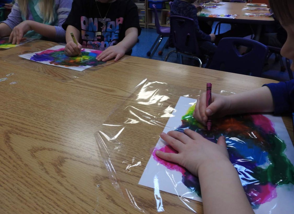 Children drawing with crayons on paper covered with plastic wrap