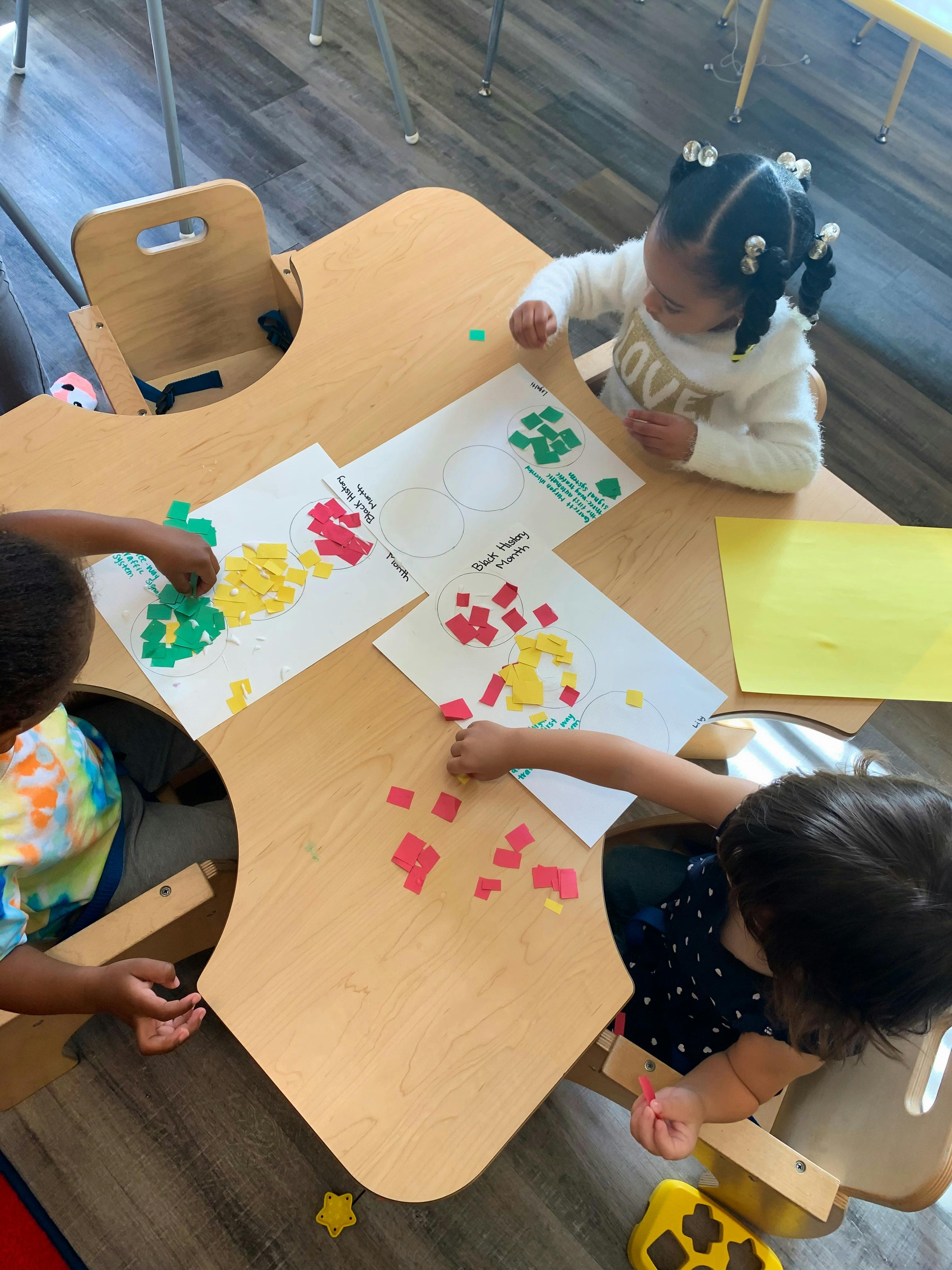 Children at a table doing an art project with paper cutouts