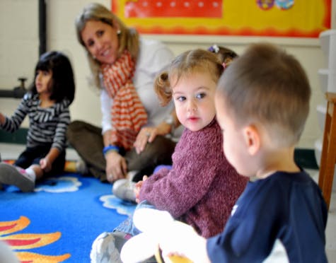 Adult and three children sitting on a blue rug in a classroom