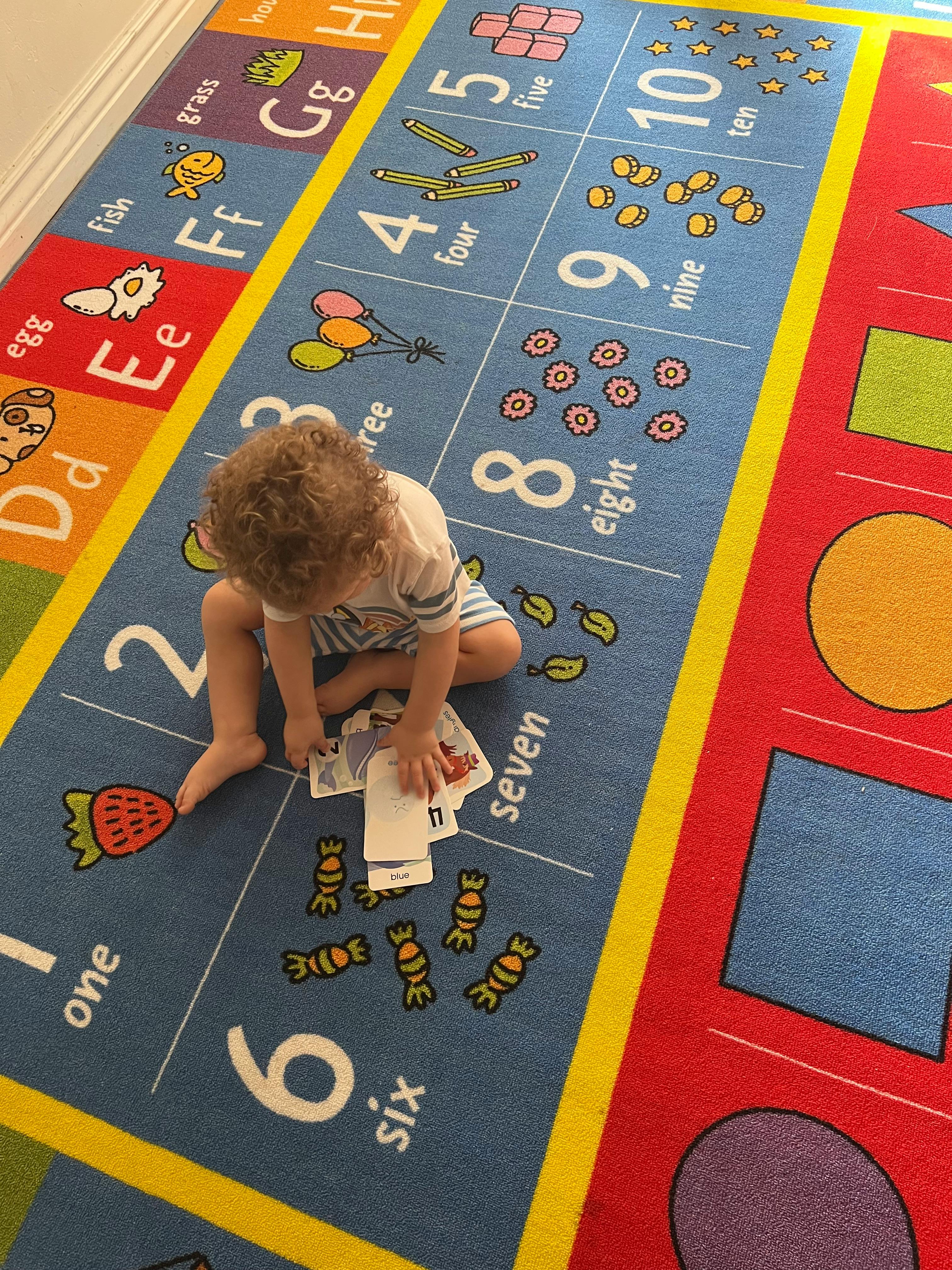 Child sitting on an alphabet and number rug, holding cards