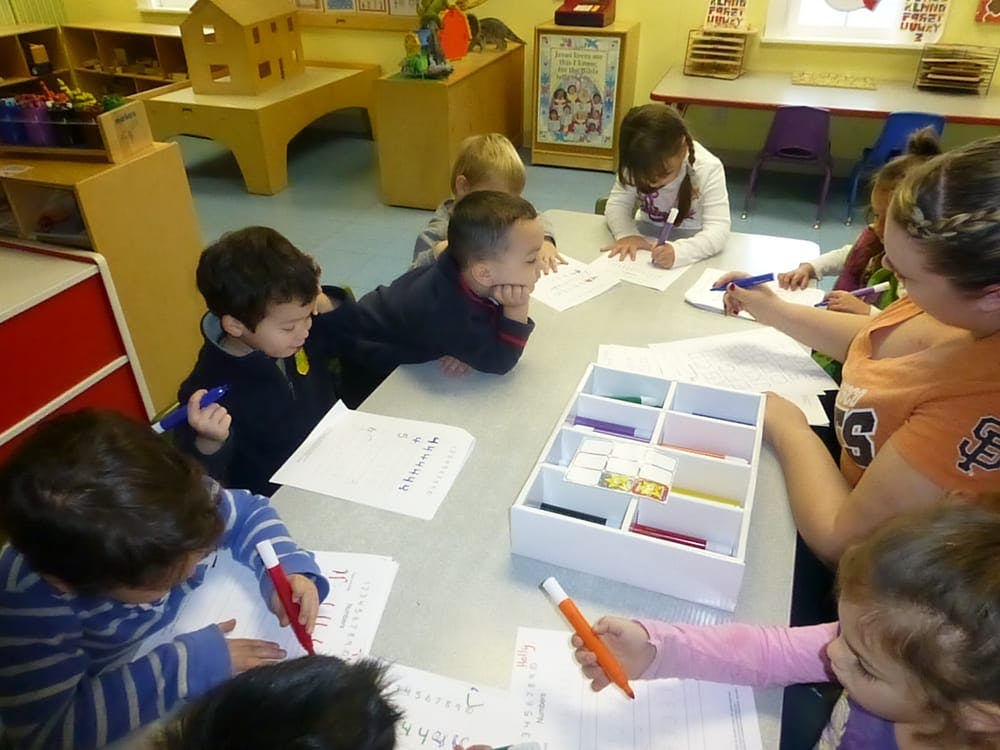 Children and an adult drawing at a table in a classroom